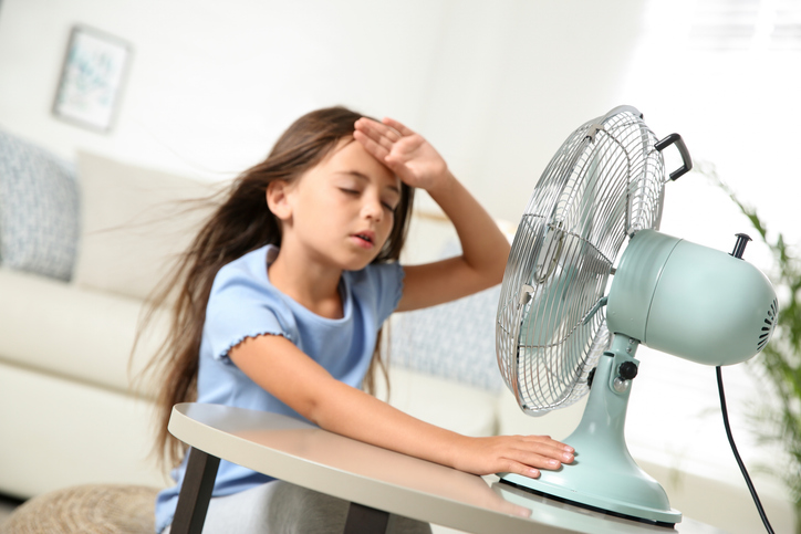 Little girl suffering from heat in front of fan at home because AC system doesn't work.